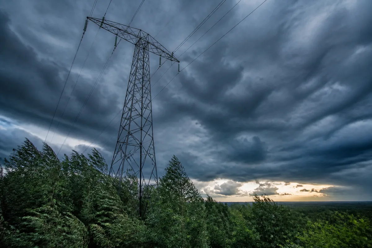 Pylône de ligne haute tension dominant une forêt sous un ciel d&rsquo;orage