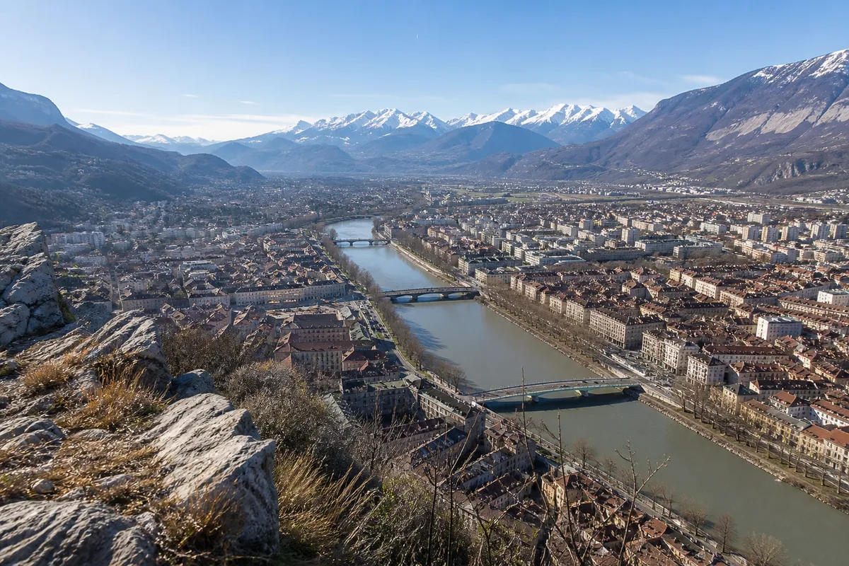 Vue plongeante sur une ville alpine traversée par une rivière, sommets enneigés à l&rsquo;horizon